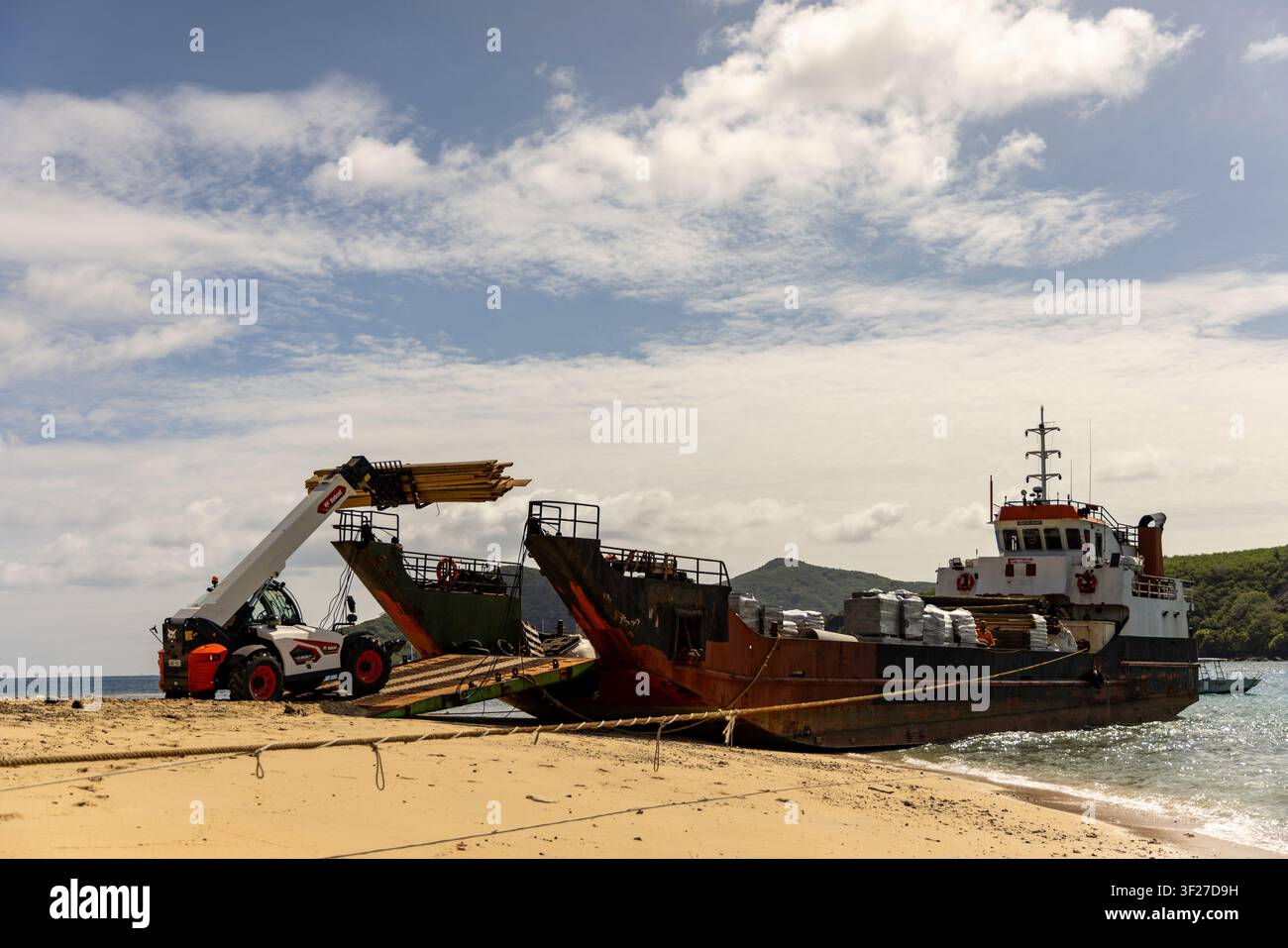 Carrello telescopico Bobcat 40.180oslp con sollevatore ad alta portata su chiatta che si ritira dalla spiaggia con una grande pila di legname in aria, fornisce la vita sull’isola Mantara Foto Stock