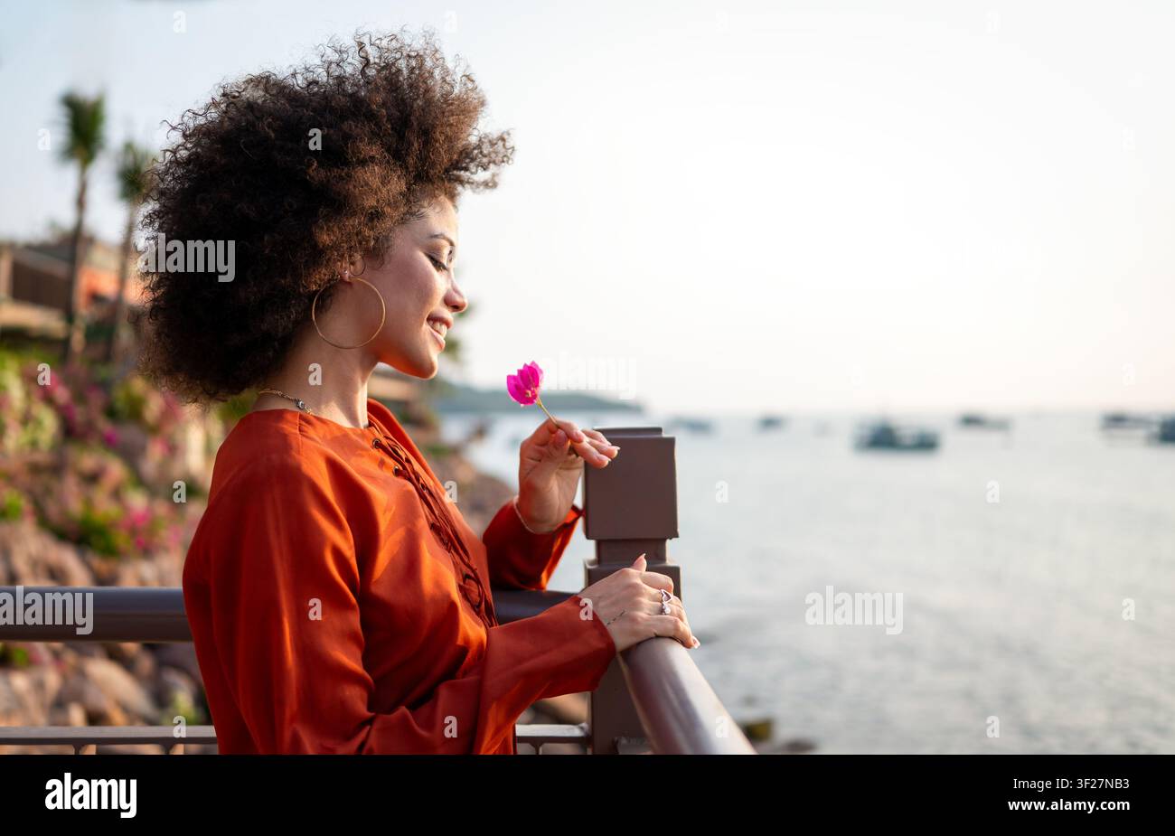 Elegante donna viaggiatrice che si rilassa in una località balneare, godendo della vista panoramica tropicale al crepuscolo Foto Stock