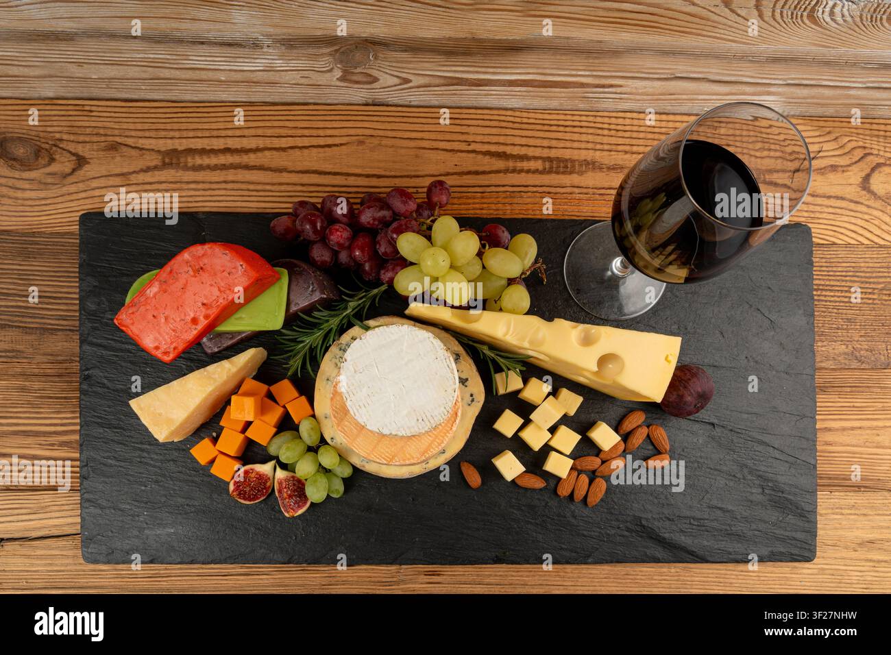 Piatto di formaggi vari colorati, piatto di gorgonzola giallo, bianco e blu con bicchiere di vino rosso, tagliere di formaggi, prodotti caseari tritati assortiti, m Foto Stock