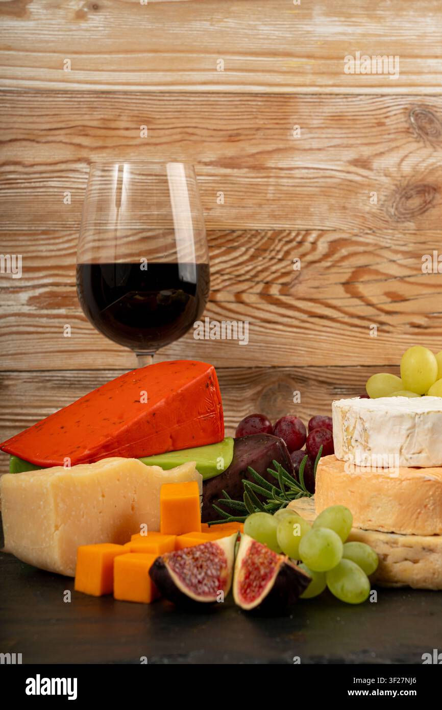 Piatto di formaggi vari colorati, piatto di gorgonzola giallo, bianco e blu con bicchiere di vino rosso, tagliere di formaggi, prodotti caseari tritati assortiti, m Foto Stock