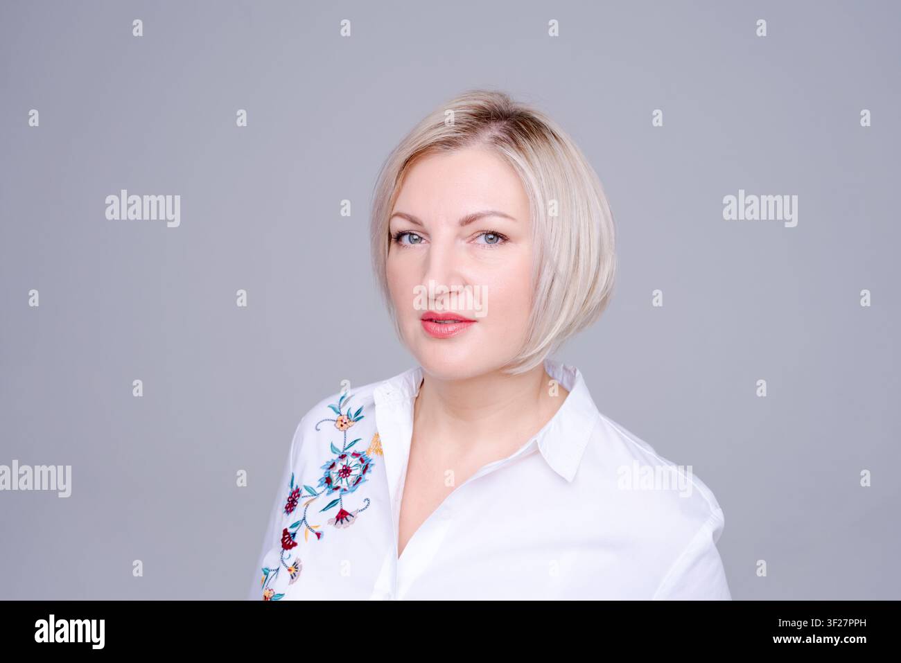 Ritratto elegante di una donna caucasica matura con espressione composta e sorriso sottile in camicia bianca in studio. Adatto per ritratto elegante, look sicuro di sé Foto Stock