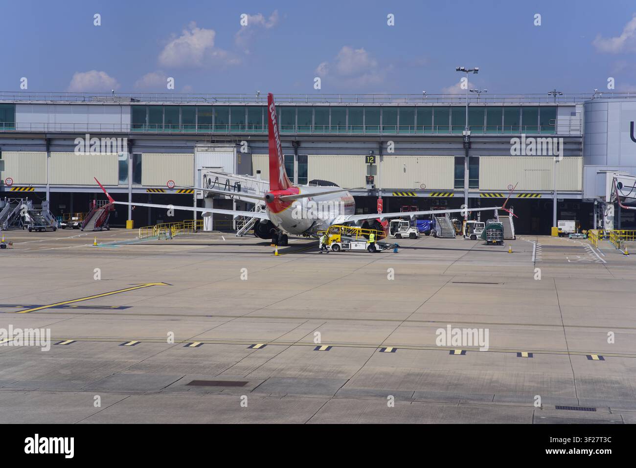 Aereo con coda rossa parcheggiato al gate del terminal con ponte di accesso in una giornata soleggiata all'aeroporto di Gatwick a Londra, Regno Unito. Foto Stock