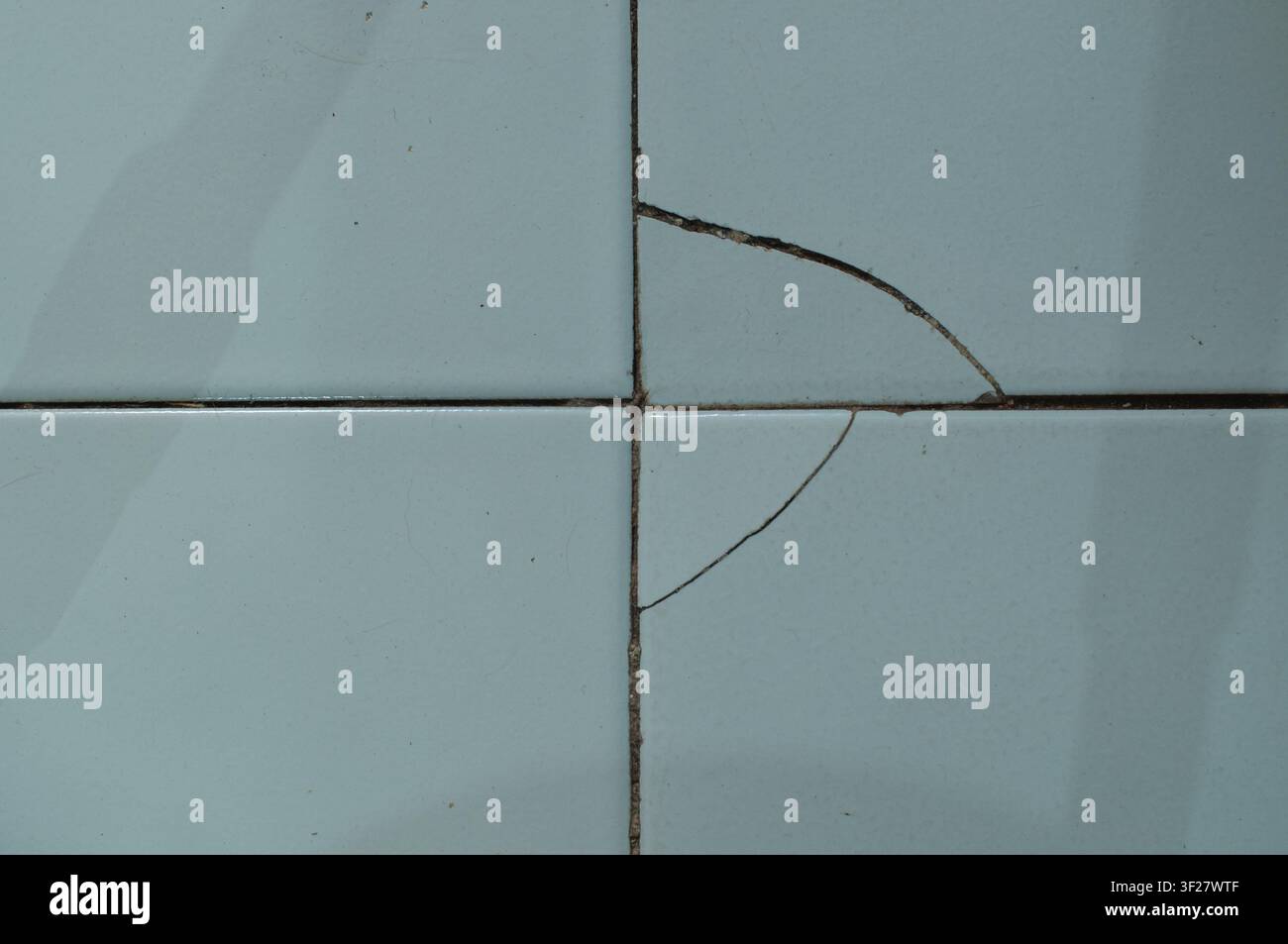 Texture dettagliata di piastrelle di ceramica rotte e scheggiate con stucco macchiato, che mostrano età, danni e usura in un bagno o in una cucina. Foto Stock