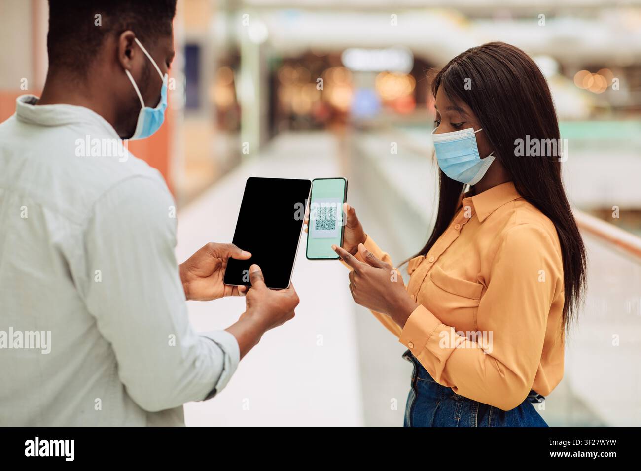 Uomo e donna neri che utilizzano smartphone e tablet con codice QR, in un centro commerciale Foto Stock