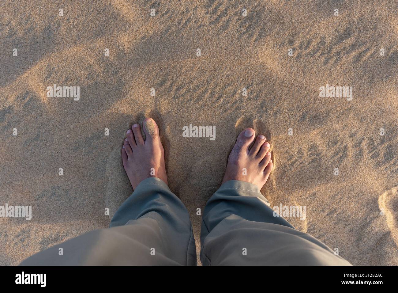 Un colpo in POV ad angolo alto di un viaggiatore in piedi a piedi nudi sulle morbide dune di sabbia dorata del Mare Interno, Khor Al Adaid, Qatar. Foto Stock
