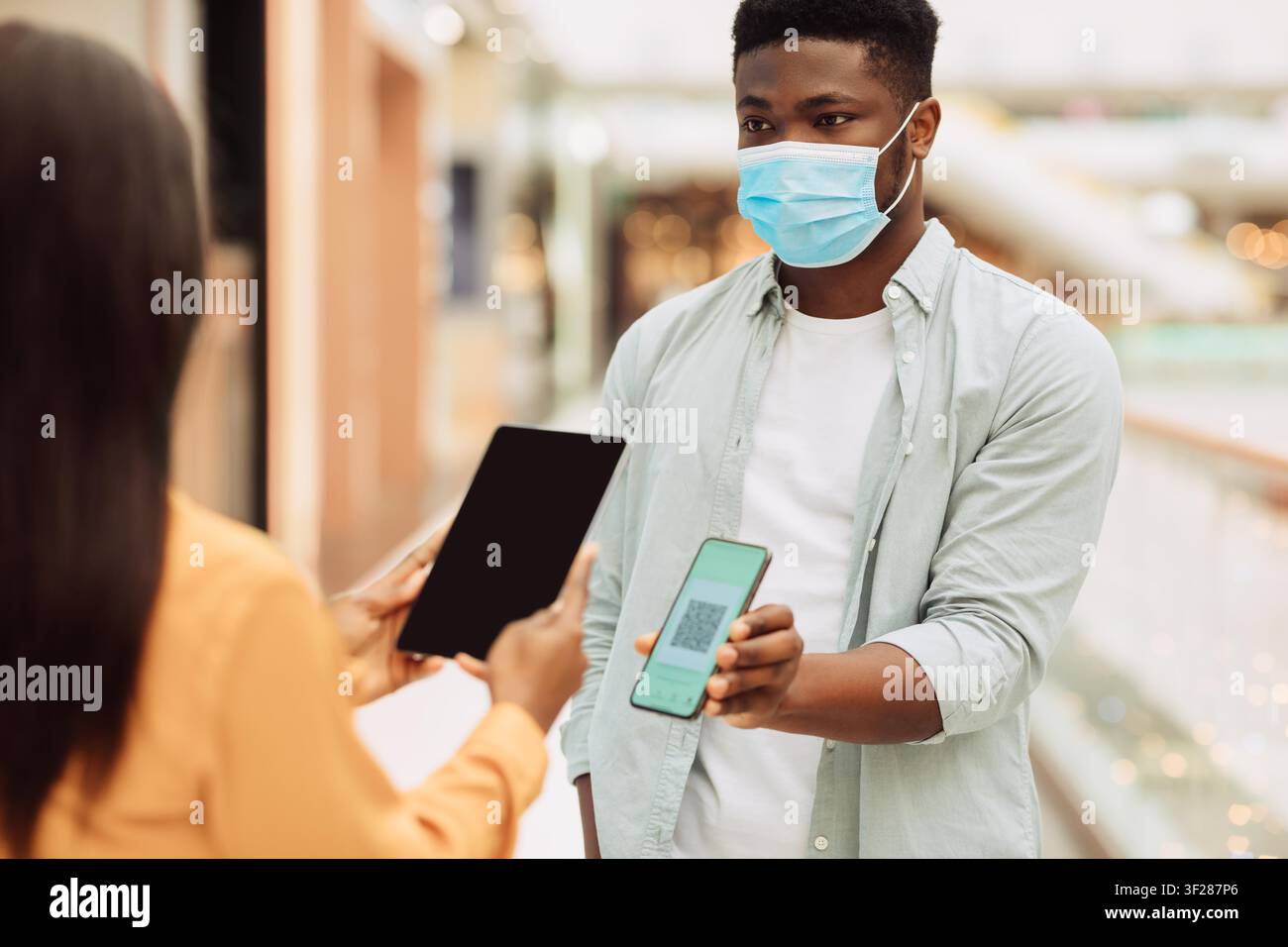 Millennial nero maschio che utilizza smartphone e tablet per pagamenti contactless in un centro commerciale Foto Stock