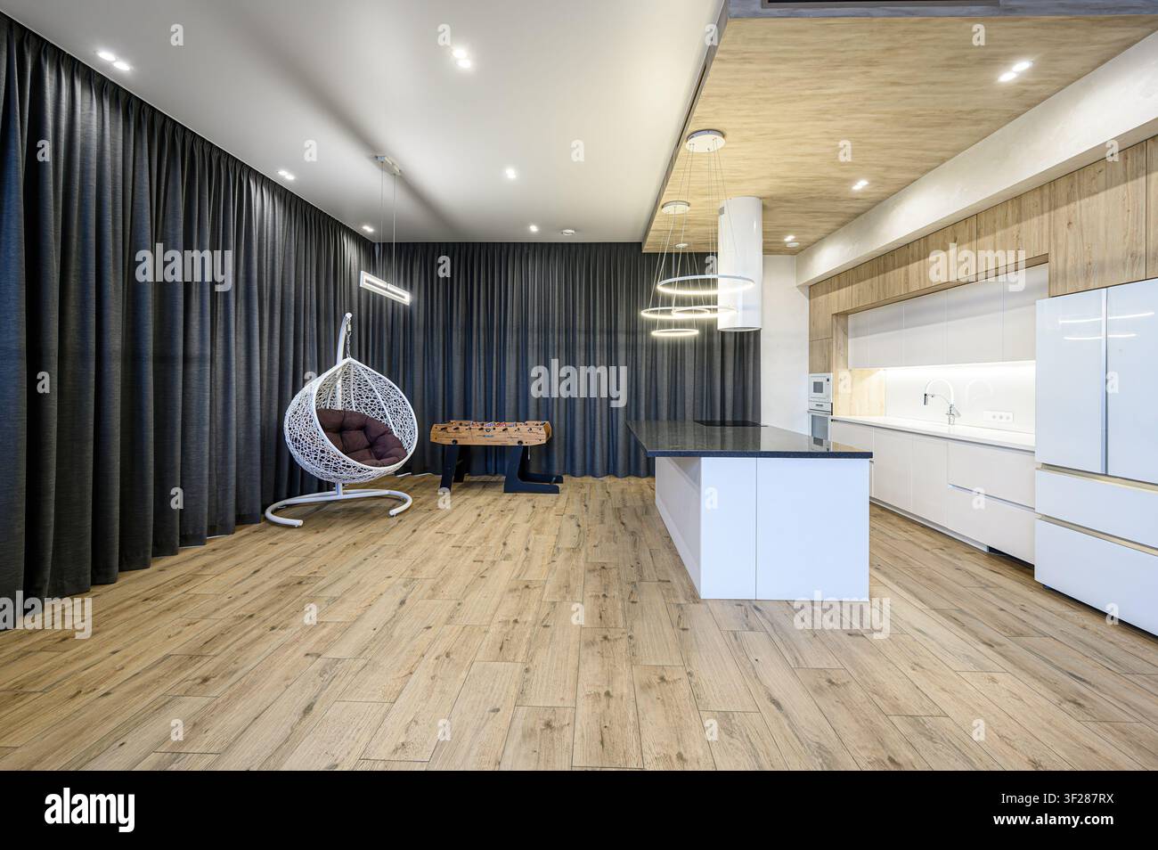 cucina e soggiorno moderni e spaziosi con una sedia a uovo bianca, un tavolo da calcetto, un'isola della cucina e pavimenti in legno chiaro Foto Stock