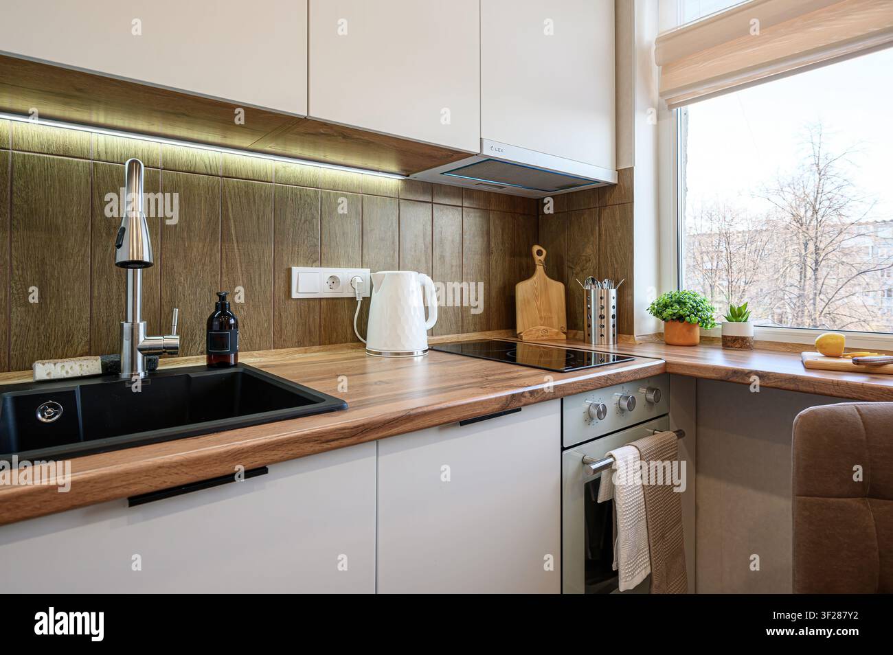 cucina moderna con armadi chiari, dettagli in legno, lavandino nero e vista dalla finestra. Spazio pulito, luminoso e funzionale Foto Stock