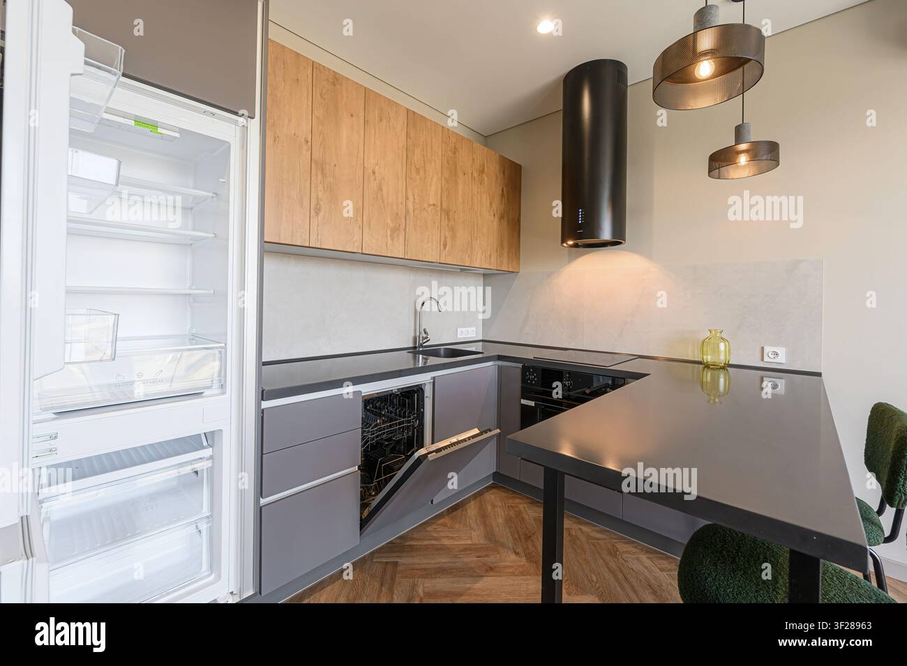 Cucina moderna con armadi grigi, dettagli in legno, frigorifero aperto, campana estraibile nera e illuminazione stilosa. Design pulito e contemporaneo Foto Stock