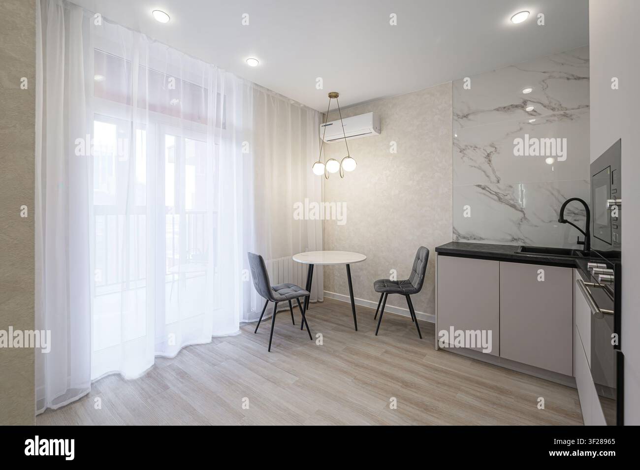 cucina moderna con un tavolo rotondo, due sedie e eleganti dettagli in marmo. Design luminoso e pulito Foto Stock