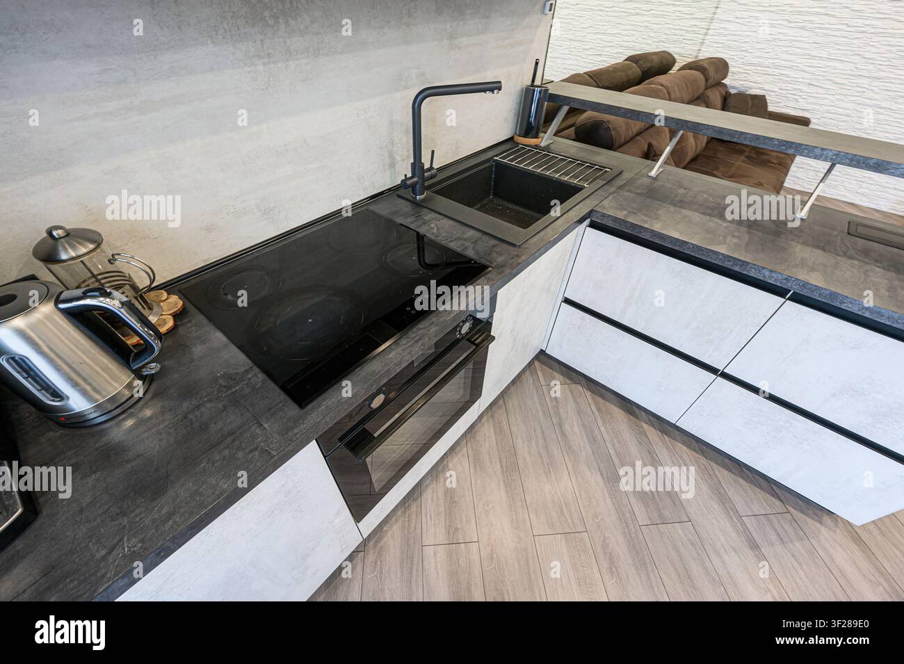 Cucina moderna con piano di lavoro scuro, fornello elettrico, lavandino e armadi bianchi eleganti con dettagli neri. È visibile anche un bollitore d'argento Foto Stock
