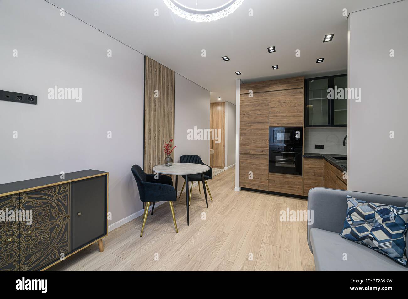 Interno di appartamento moderno con accenti in legno, un tavolo da pranzo e un'anticipazione della cucina. Linee pulite e colori neutri Foto Stock