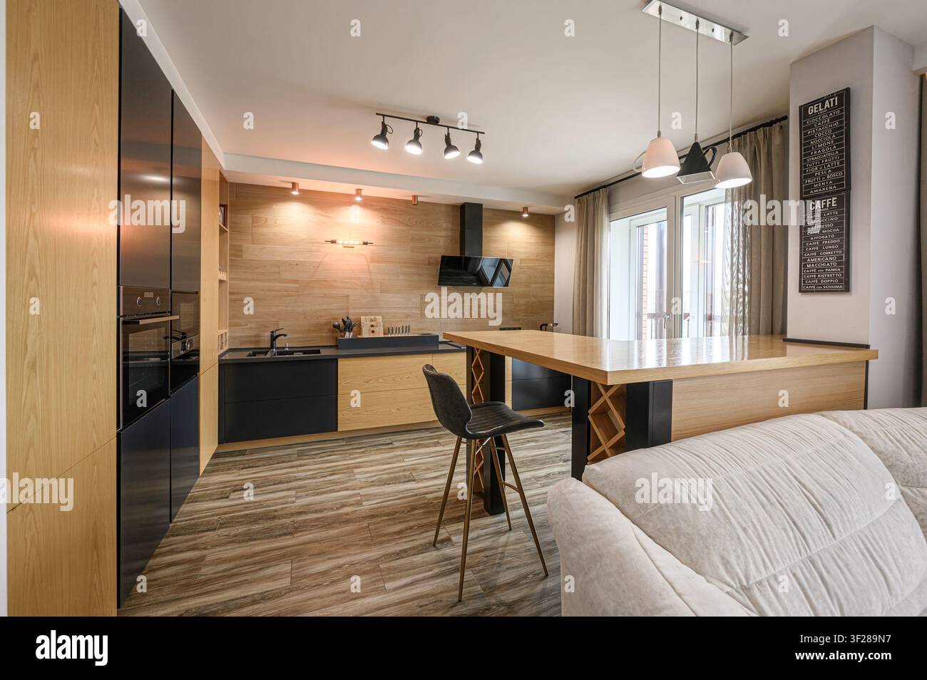 Interno di cucina moderna con armadi in legno, dettagli neri, isola con posti a sedere al bar e luce naturale Foto Stock