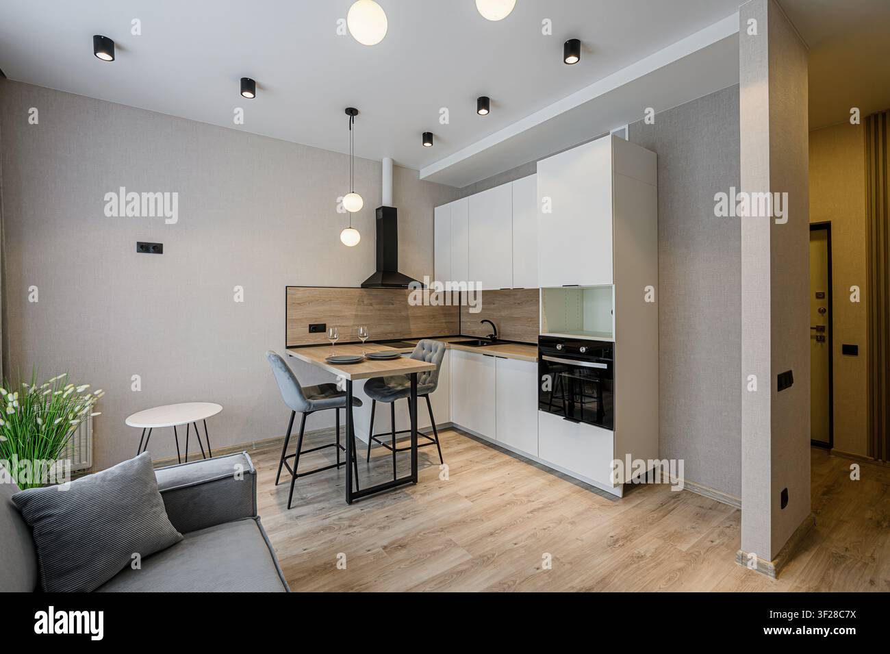 Cucina-soggiorno moderna con armadi bianchi, dettagli in legno, divano grigio e illuminazione elegante Foto Stock