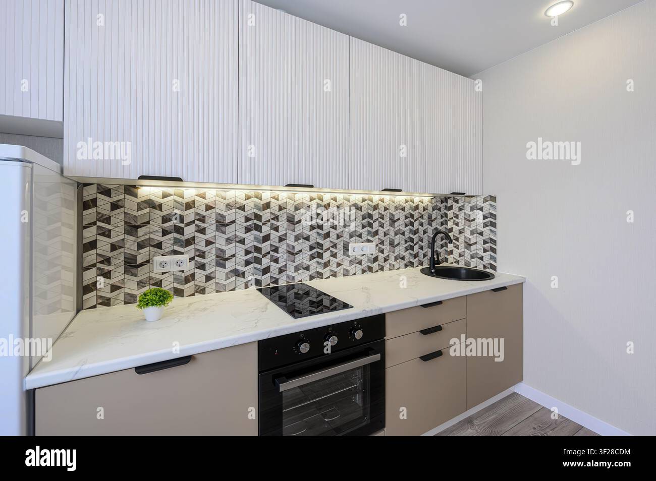 Cucina moderna con armadi bianchi testurizzati sopra un piano a smalto a motivi marmorizzati. Gli armadi inferiori sono marrone chiaro con dettagli neri Foto Stock