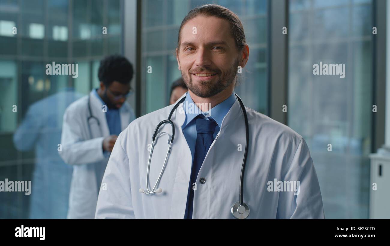 Ritratto di un uomo caucasico medico sorridente in uniforme medica che posa in clinica. Pediatra maschile, terapista, praticante, chirurgo, professionista della medicina Foto Stock