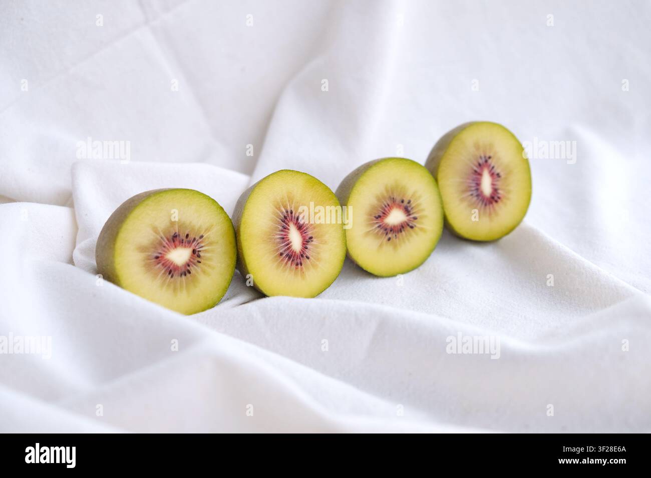 Metà del kiwi rosso su uno sfondo tessile di colore chiaro. Foto Stock