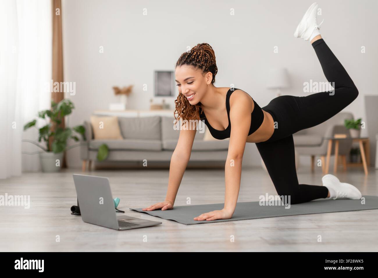 Giovane donna nera felice che si allena a casa, utilizza un laptop, concetto di esercizio fisico Foto Stock