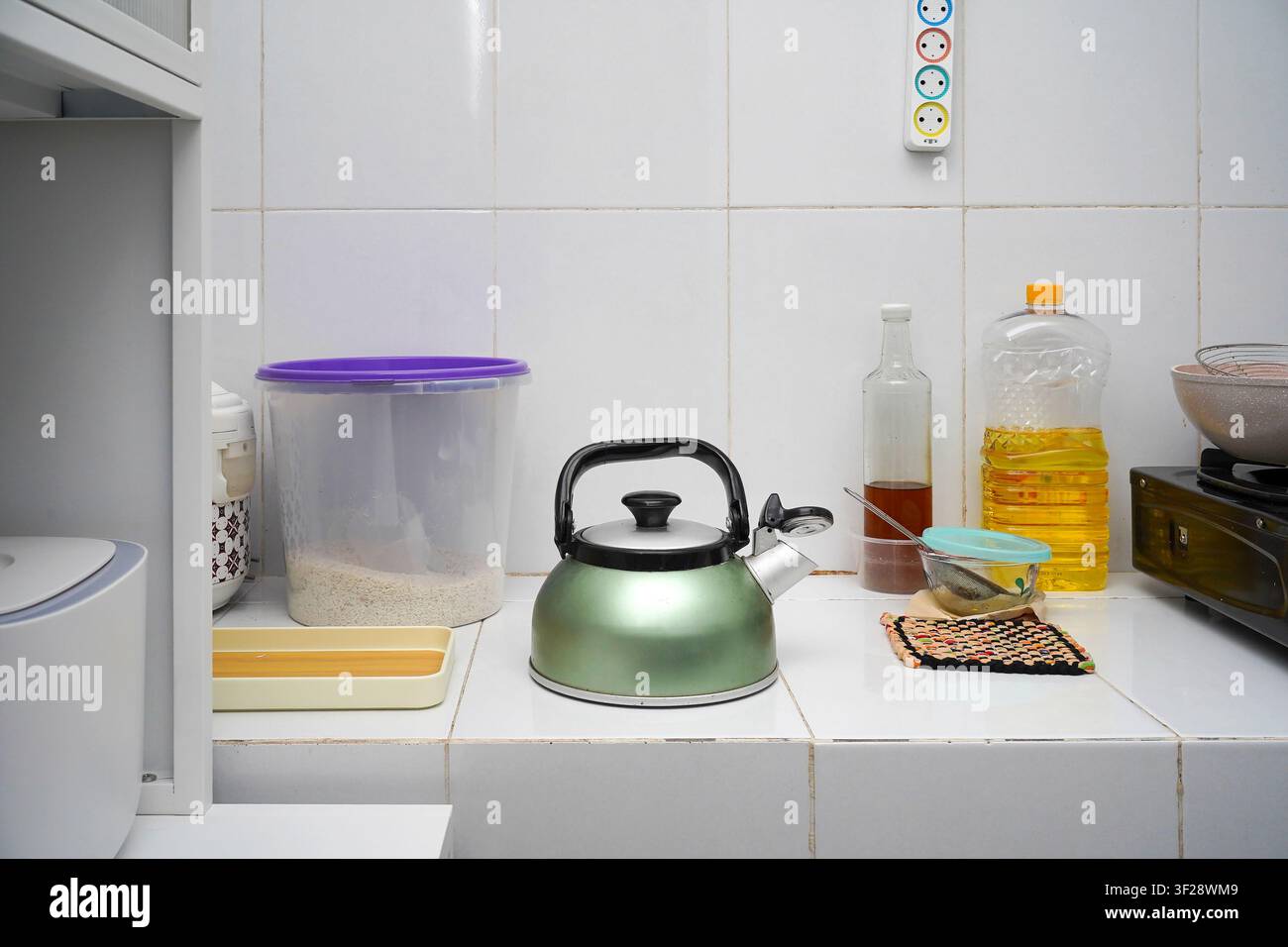 Piano di lavoro della cucina con bollitore, contenitore per il riso, olio da cucina e articoli per la preparazione del cibo. Concetto di cucina quotidiana e di gestione della casa. Foto Stock