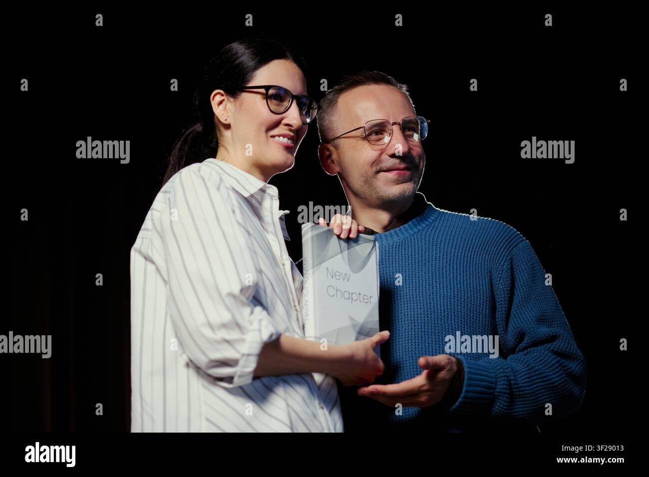 Inquadratura media di donna e uomo caucasici di mezza età che tengono un libro e presentano una pubblicazione sul palco, suggerendo autorevolezza e risultato. Ideale per editoria, istruzione, marketing di eventi di oratoria Foto Stock