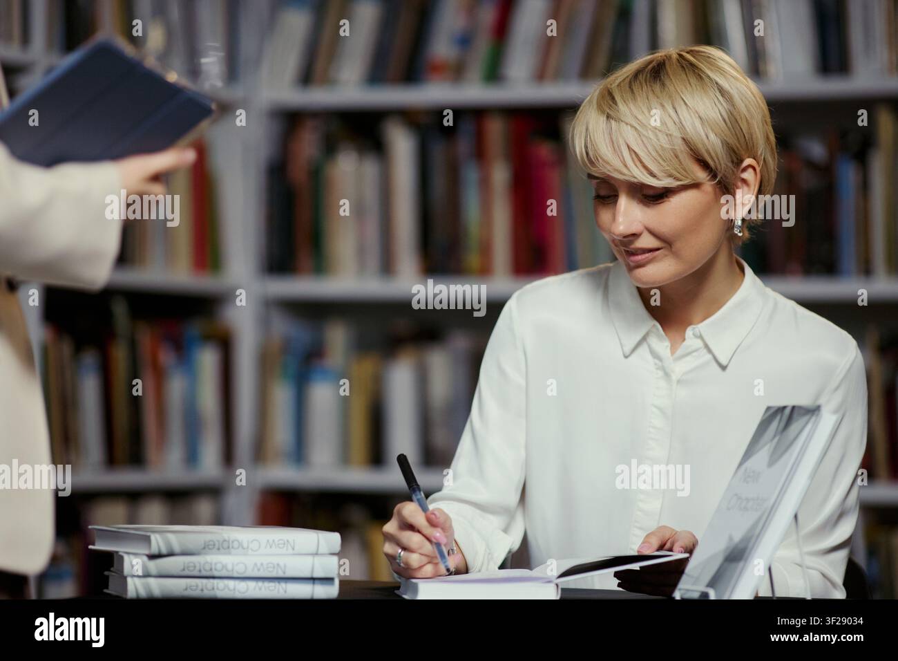 Giovane donna caucasica che autografa un libro a un evento in libreria, promuovendo il marketing dell'autore e l'impegno dei lettori. Utilizzo commerciale per il marketing editoriale, la promozione letteraria, campagne editoriali Foto Stock