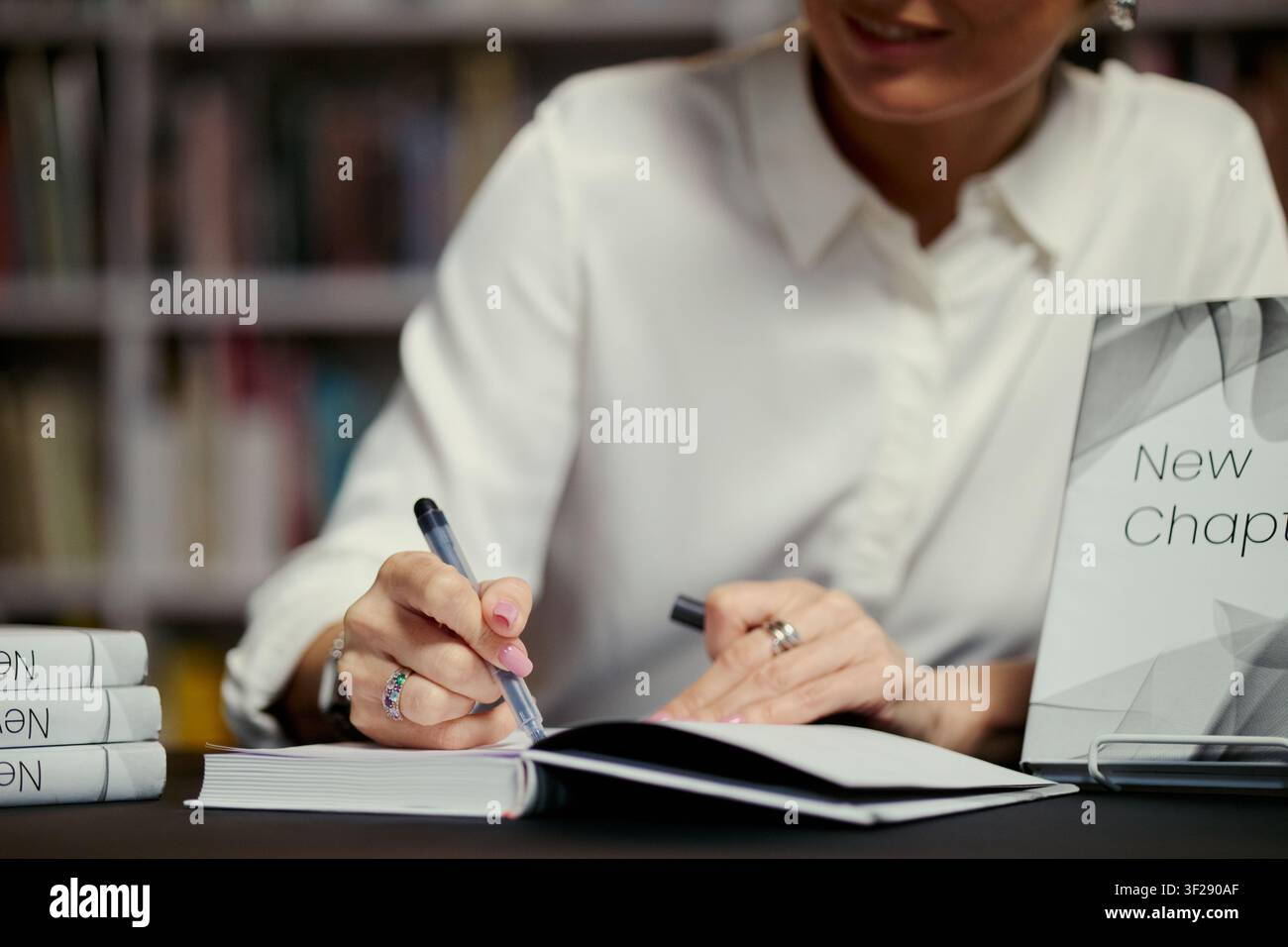 Primo piano di una giovane donna che autografa un libro in una libreria o in una biblioteca, promuovendo l'editoria e il branding dell'autore. Adatto per il marketing del lancio di libri, campagne editoriali, uso redazionale Foto Stock