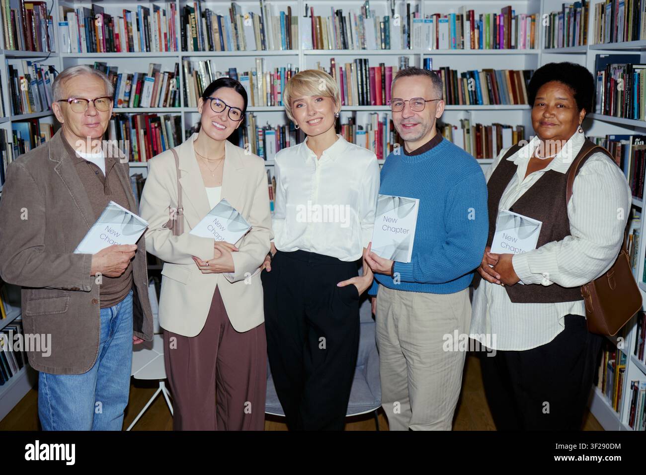 Ritratto di membri adulti diversificati di un club del libro che tengono romanzi e stanno in una biblioteca, promuovendo la comunità di lettura e la cultura letteraria. Ideale per il marketing educativo e le campagne editoriali Foto Stock