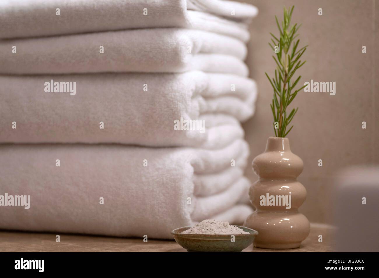 Asciugamano bianco arrotolato su un vassoio da bagno in legno con articoli per il benessere in un bagno moderno di hotel, creando un'atmosfera rilassante di benessere Foto Stock