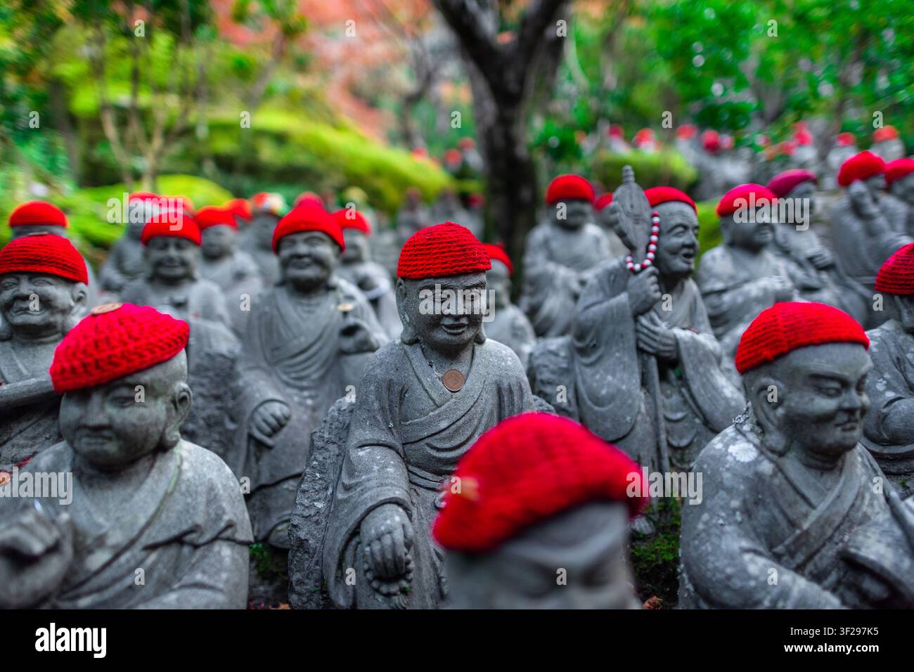 Le statue di Jizo Bosatsu, figure guardiane buddiste con cappelli rossi, sono disposte lungo il sentiero che porta al tempio Daisho-in sull'isola di Miyajima, in Giappone. Foto Stock