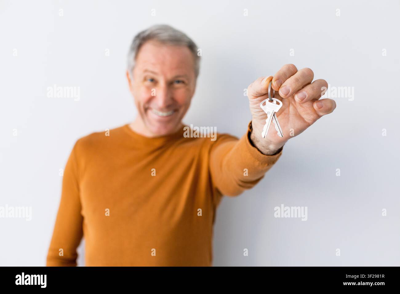 Uomo anziano caucasico felice che tiene le chiavi con un sorriso, ambiente domestico, concetto immobiliare Foto Stock