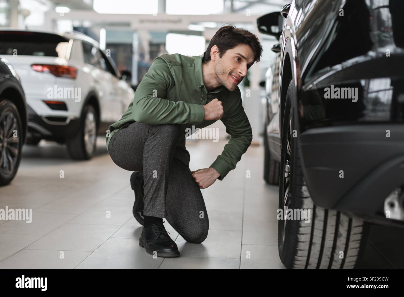 Giovane uomo concentrato che ispeziona un pneumatico dell'auto in un concessionario, concetto aziendale Foto Stock