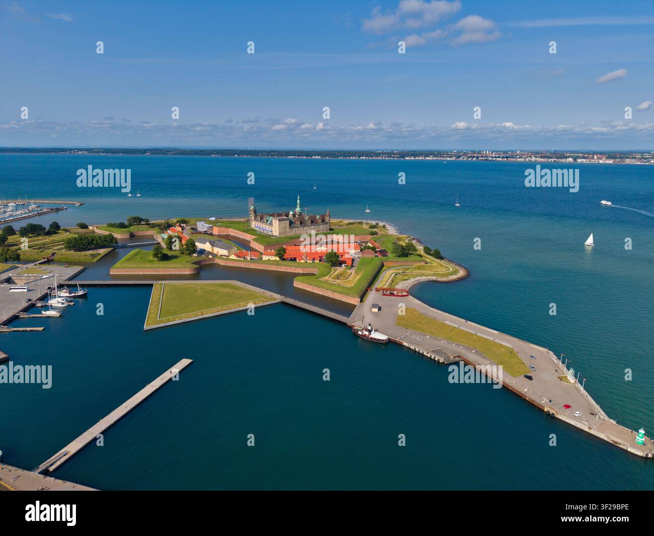 Vista aerea del castello di Kronborg, una fortezza storica circondata da fossati e bastioni verdi, situata sulla costa con un porto e il mare blu sotto un c Foto Stock