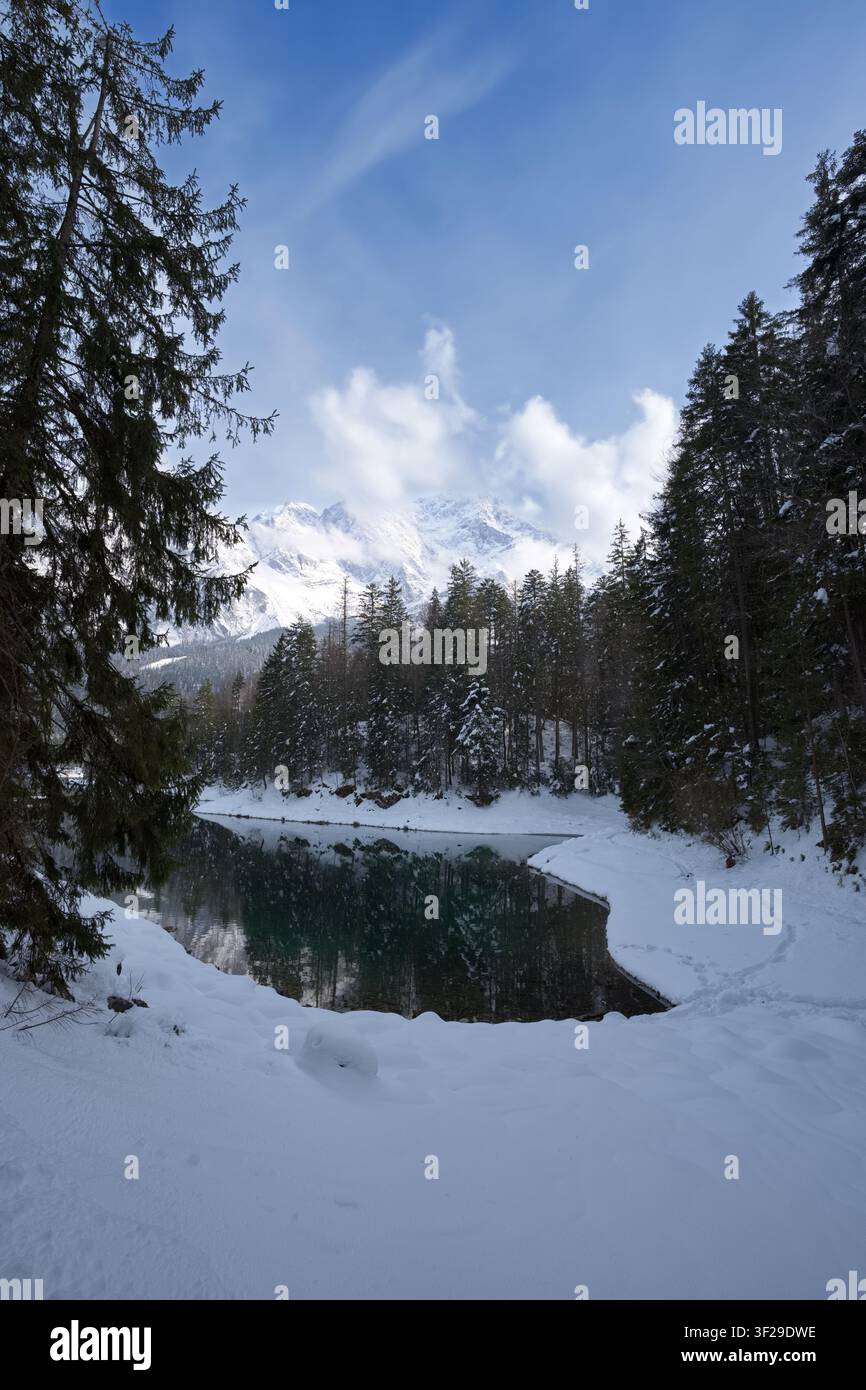 Una bellissima ripresa verticale dell'acqua turchese incontaminata del lago Eibsee in inverno, con la sua riva innevata, pini e abeti coperti di ghiaccio, e un Foto Stock