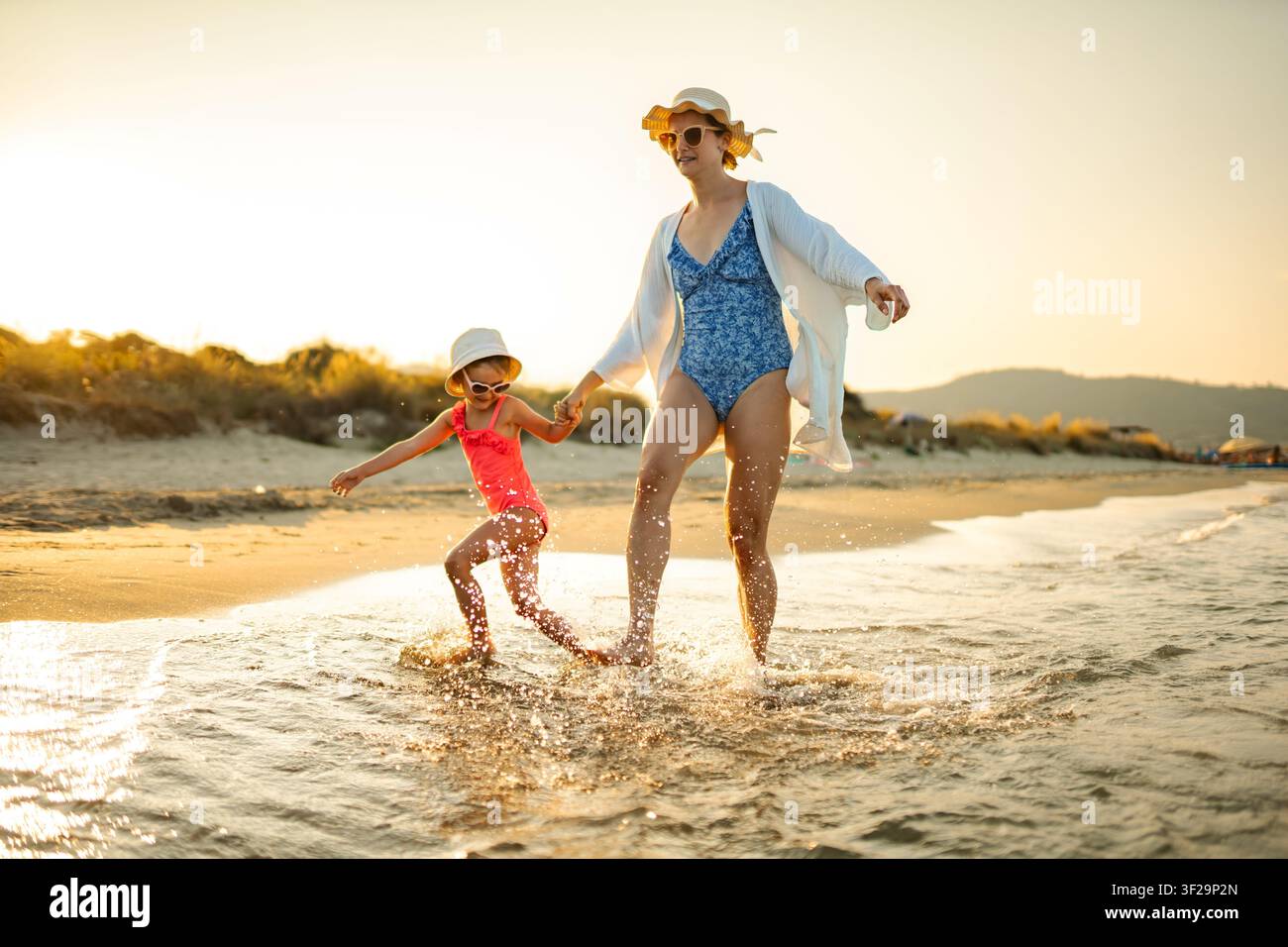 Madre e figlia che schizzano acqua durante una vacanza estiva in spiaggia al tramonto Foto Stock
