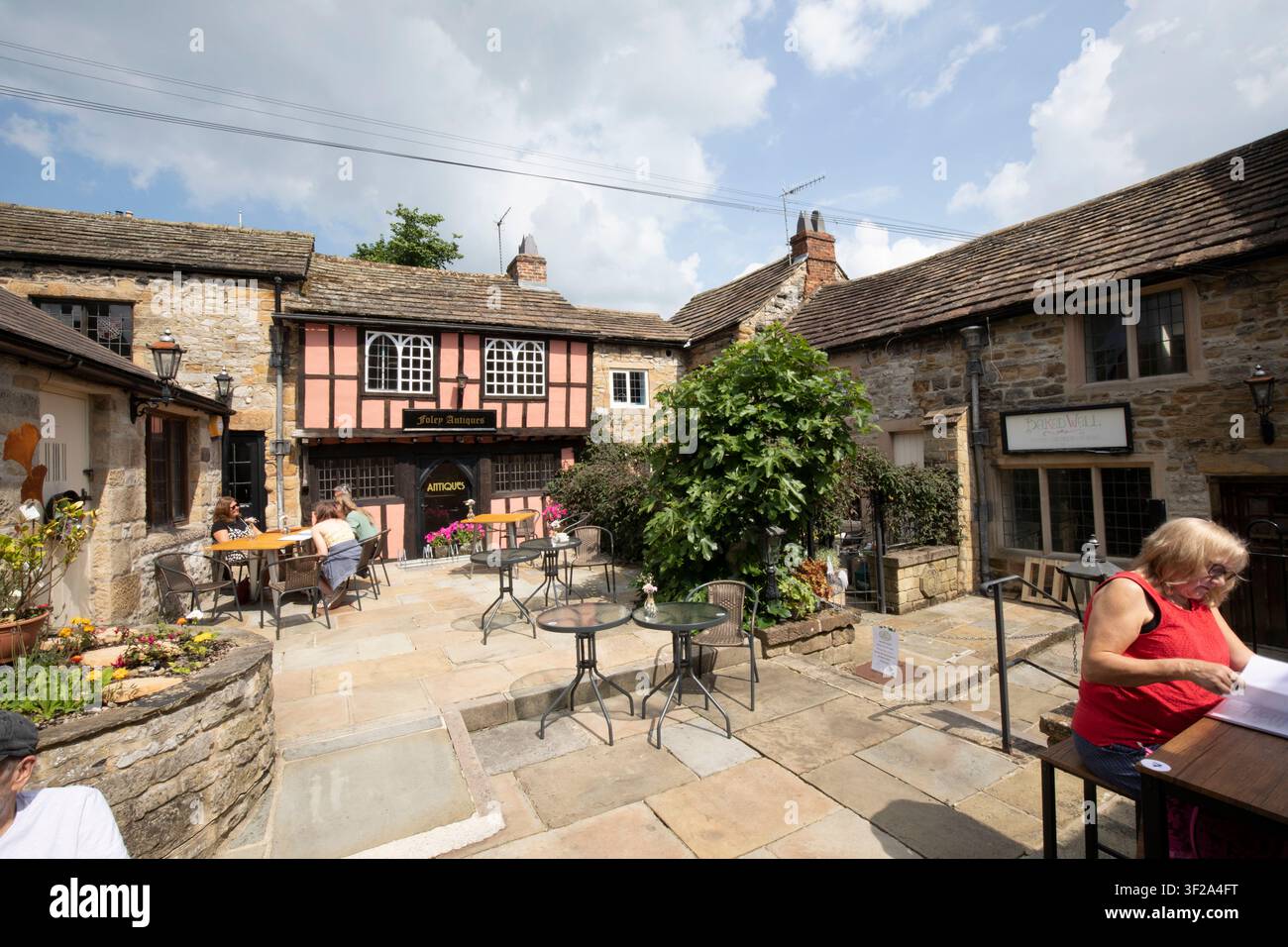 Turisti che si rilassano in un caffè all'aperto circondati da edifici storici in pietra e in legno a King's Court, Bakewell, Derbyshire, Regno Unito. Foto Stock