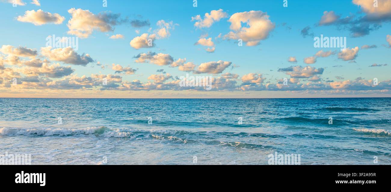 Tramonto sulla spiaggia con onde calme e soffici nuvole nel cielo. Foto Stock