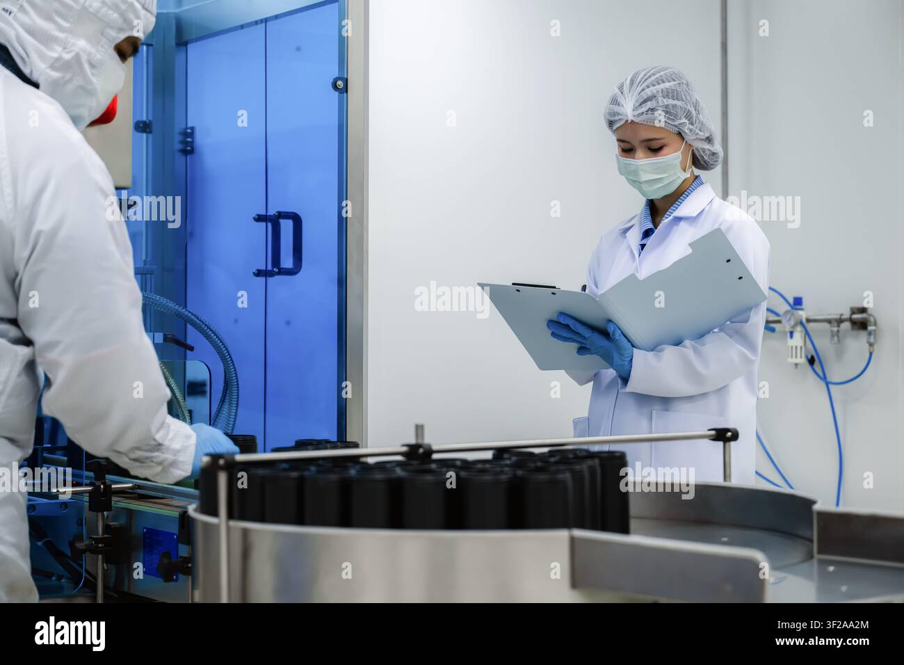 Ricercatore di laboratorio in fabbrica che controlla e scrive un rapporto di qualità su una clipboard vicino alla linea di produzione di medicinali. concetto di farmaceutica Foto Stock