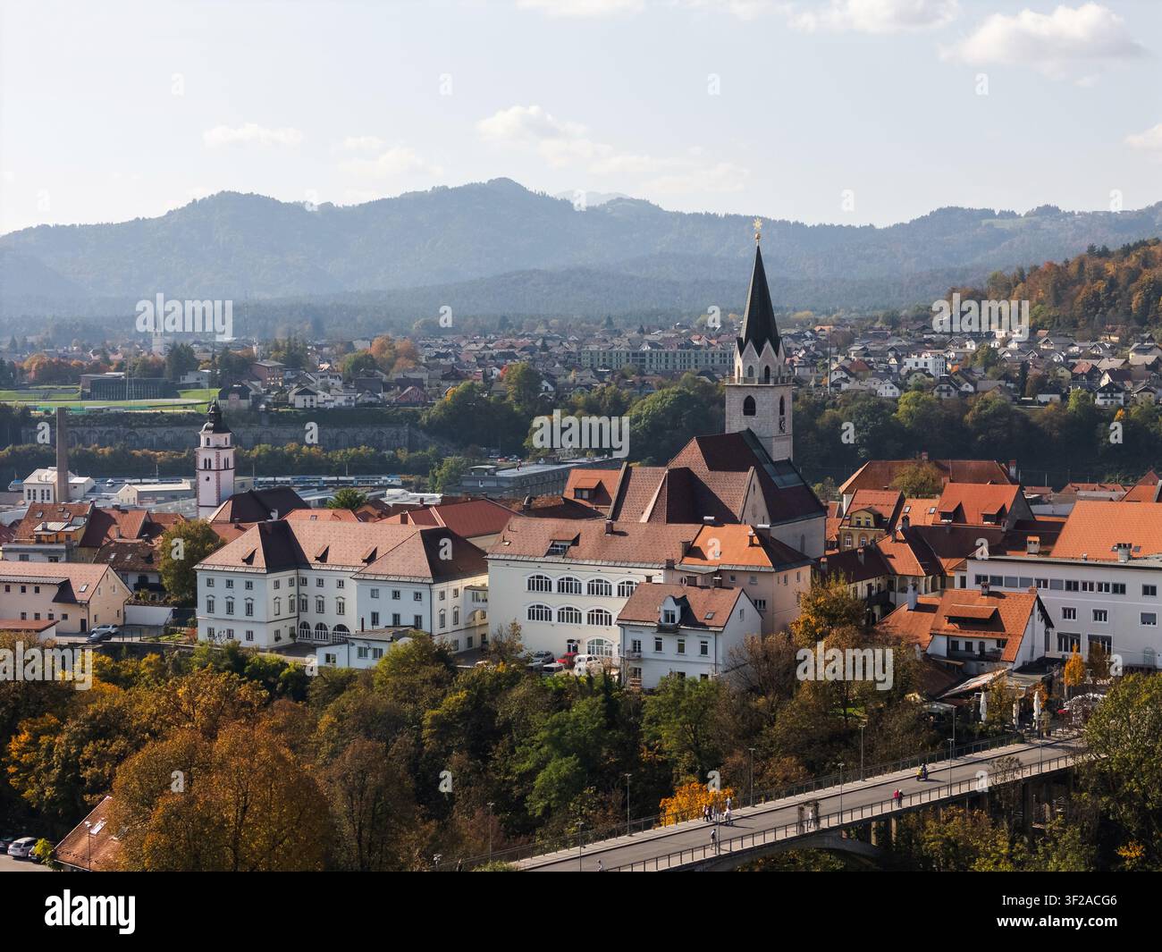 Una vista aerea mostra Kranj, in Slovenia, con la sua vecchia città medievale, le torri delle chiese e il paesaggio circostante. Un cielo blu terso evidenzia la scena. Foto Stock