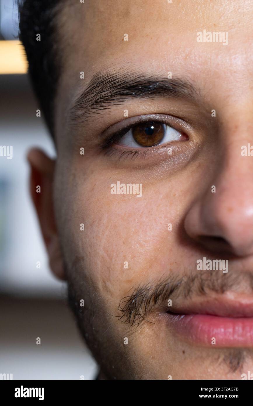 Uomo africano che guarda verso la fotocamera in studio con mensola sfocata, mostra occhio marrone, banda di luce calda Foto Stock