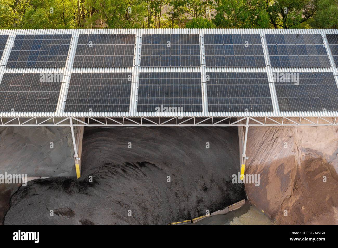 Vista aerea di pannelli solari installati su una struttura di tetto che copre grandi cumuli di materiale industriale scuro in Polonia. Foto Stock