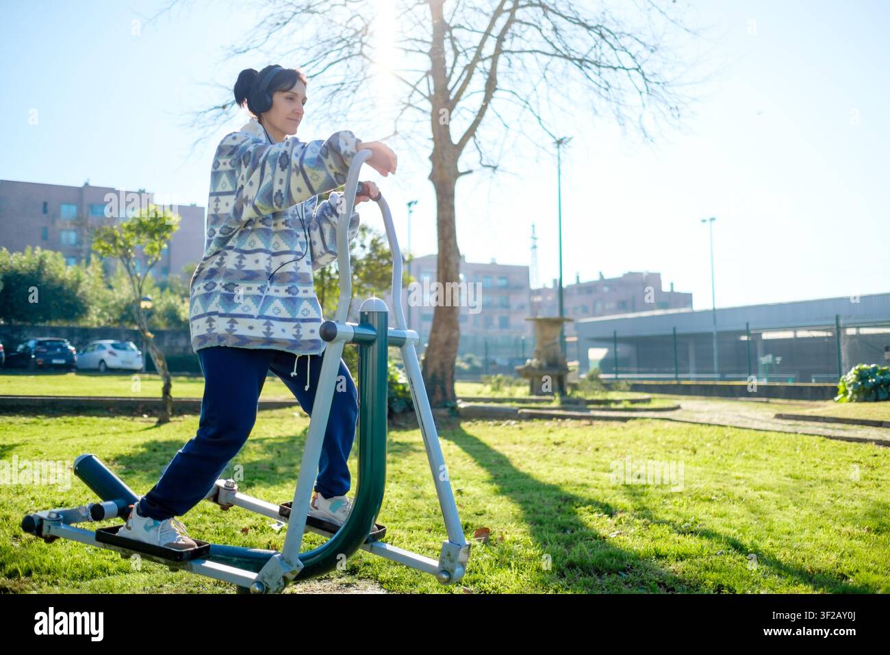Donna con cuffie che fa un allenamento di fitness in un parco pubblico in una giornata soleggiata Foto Stock