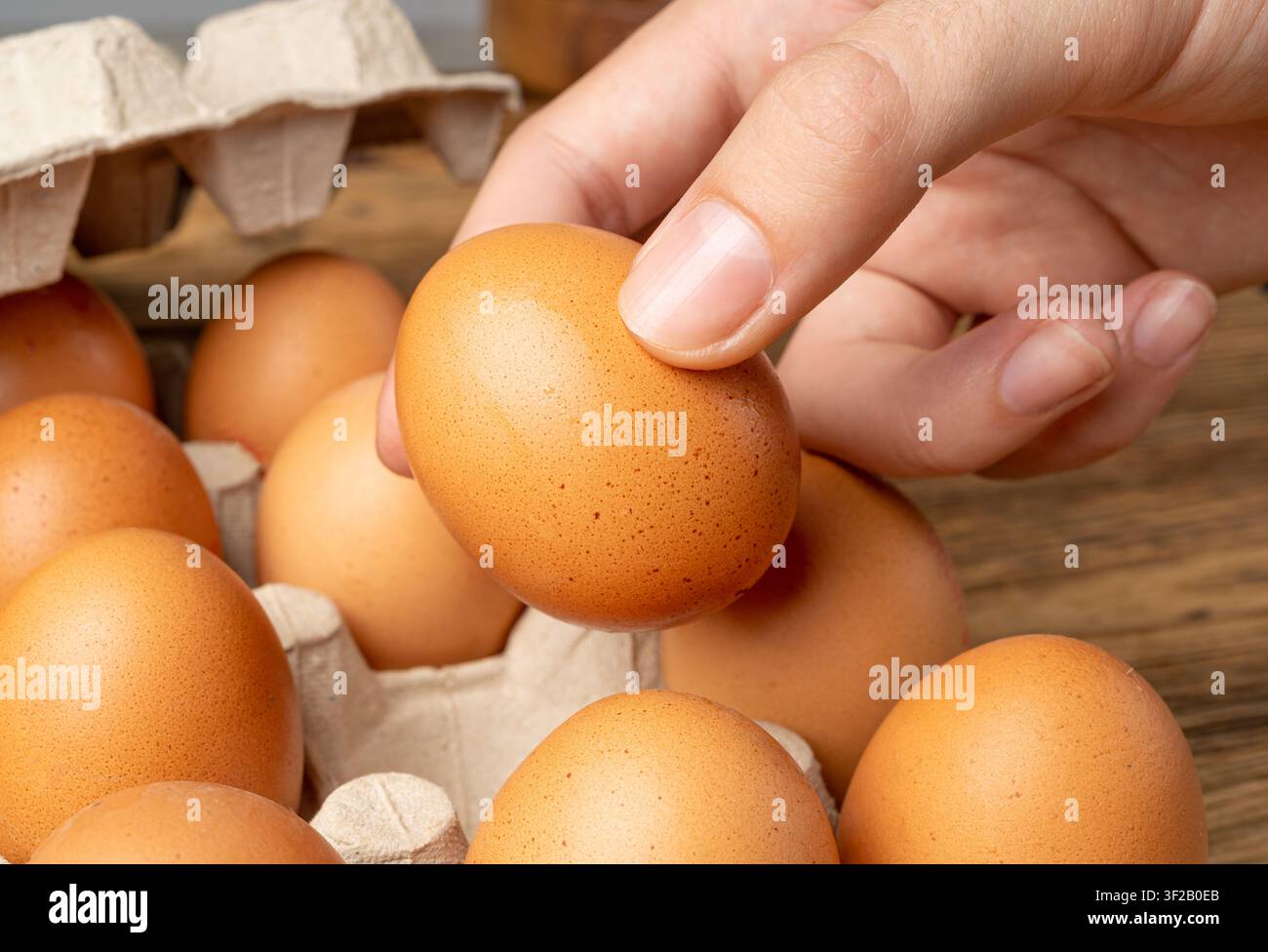 Mano che tiene uova di pollo crude sopra uno sfondo di tavolo di legno, prende un uovo bio marrone, shopping, confezione in scatola di cartone in primo piano Foto Stock