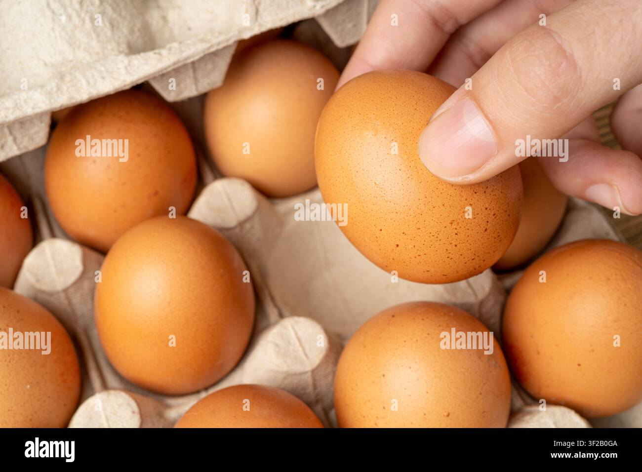 Mano che tiene uova di pollo crude sopra uno sfondo di tavolo di legno, prende un uovo bio marrone, shopping, confezione in scatola di cartone in primo piano Foto Stock