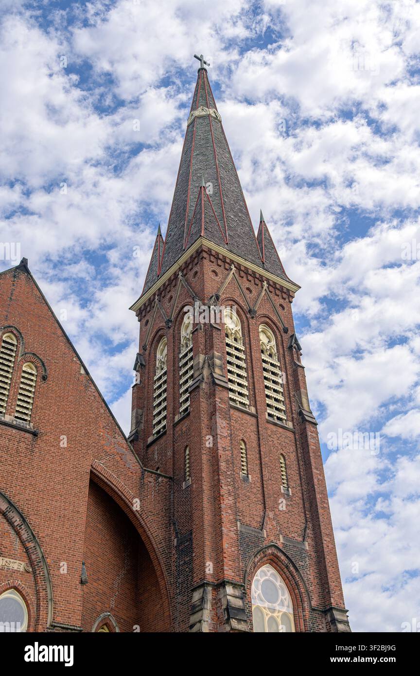 Campanile della chiesa con croce sotto un cielo blu pieno di nuvole sparse. Caratteristica architettonica della First Baptist Church. Foto Stock