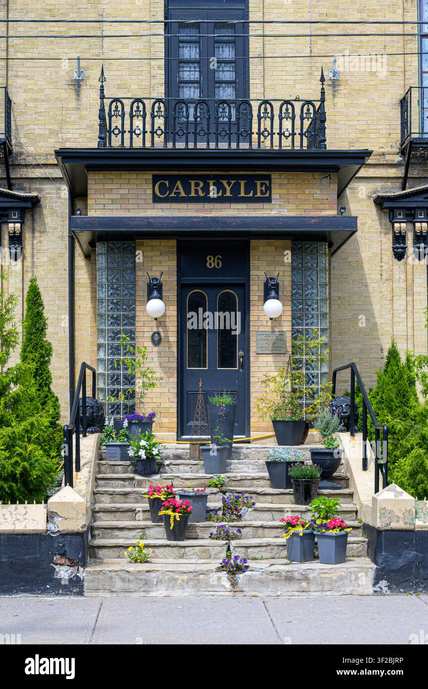 Ingresso dell'edificio dell'hotel Carlyle con porta nera, gradini in pietra, vasi di fiori e balcone in ferro decorativo. Foto Stock