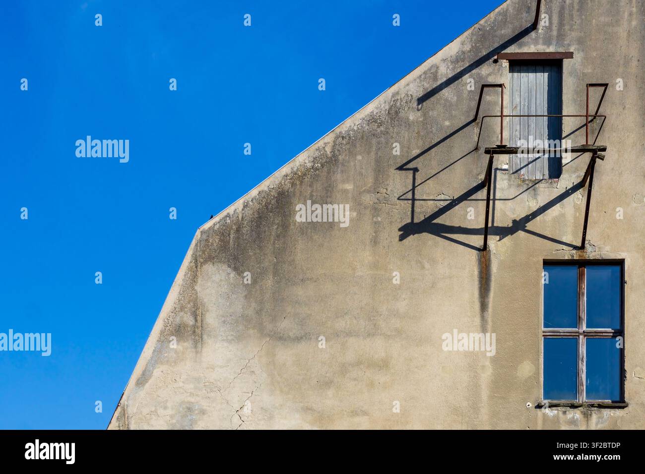 Facciata erosa di un vecchio edificio con una porta in legno rialzata e una piccola piattaforma in metallo e cielo blu. Brandmauer, Firewall, Architettura. Foto Stock