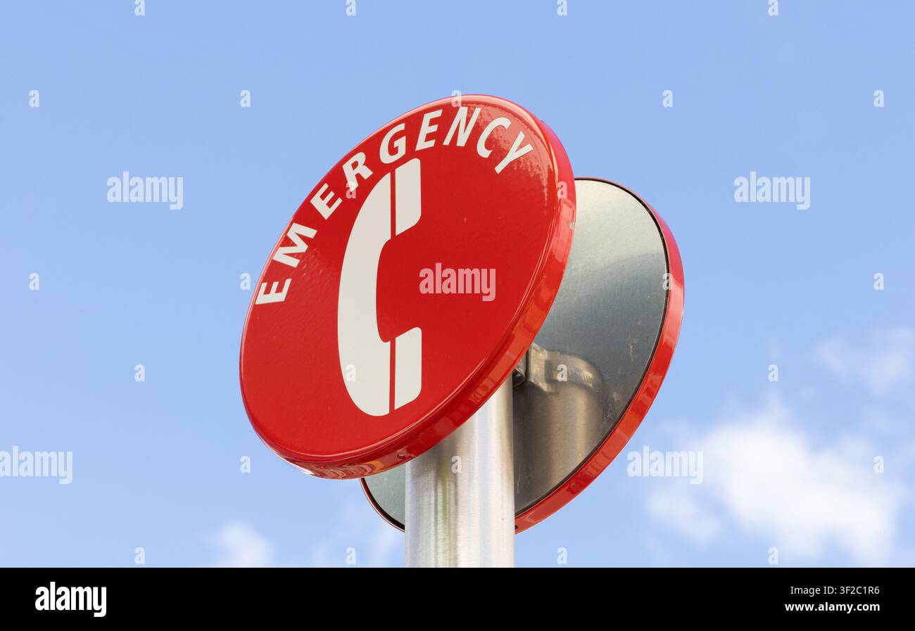 Vista ad angolo basso di un cartello telefonico di emergenza su un palo metallico contro un cielo azzurro con leggere nuvole. Foto Stock