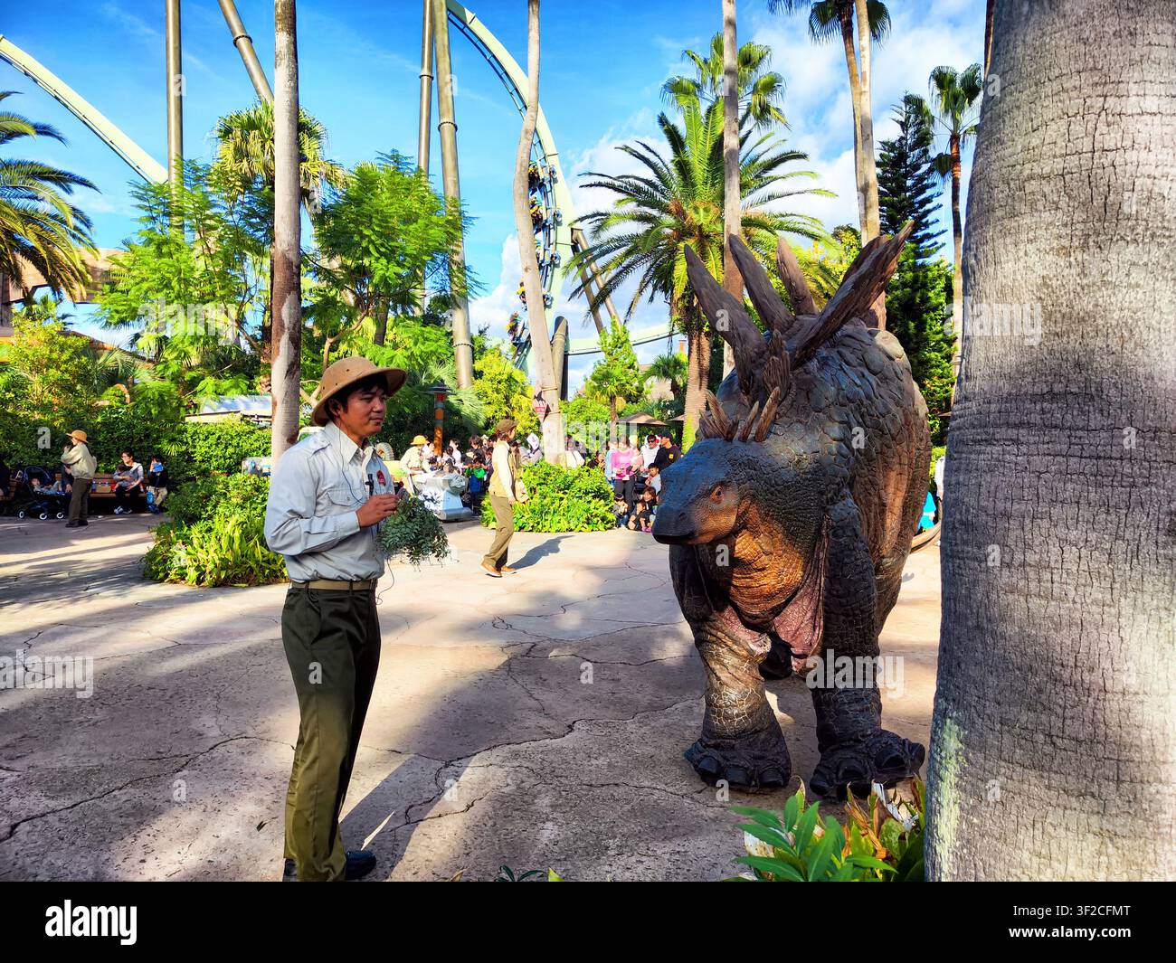 Giappone, Osaka – 28 ottobre 2024: Gli ospiti godono di un vivace incontro con un personaggio dinosauro in un'area soleggiata del Universal Studio Park, circondati da pal Foto Stock