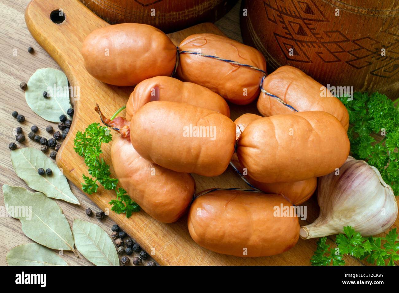 Un mazzo di piccole salsicce affumicate su un tagliere di legno. Salsicce tradizionali con spezie ed erbe. Foto Stock