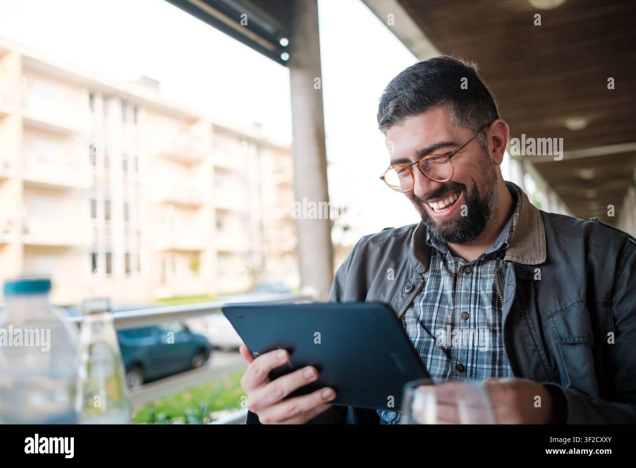Uomo che ride guardando contenuti su un tablet digitale in un caffè all'aperto Foto Stock